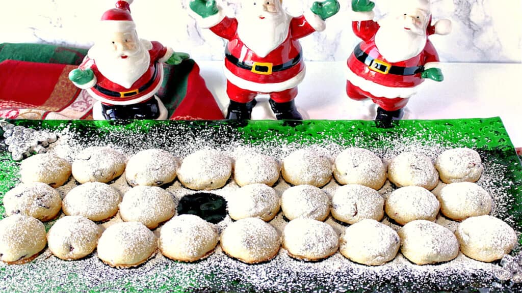 A horizontal image of snowball cookies on a green glass holiday plate dusted with confectioners sugar with one cookie missing.