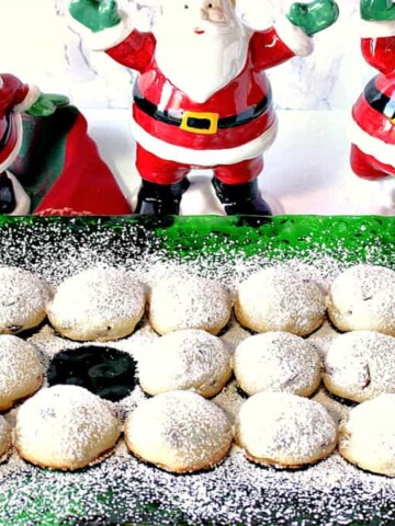 A horizontal image of snowball cookies on a green glass holiday plate dusted with confectioners sugar with one cookie missing.