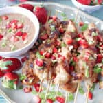 A platter filled with Chicken with Strawberry Satay Sauce in a dish with green onions and diced strawberries as garnish.