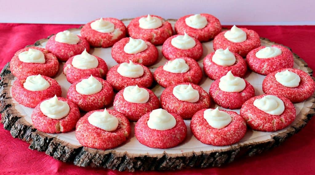 A rustic wooden tray filled with red Cream Cheese Cookies with Creamy Cheesecake topping