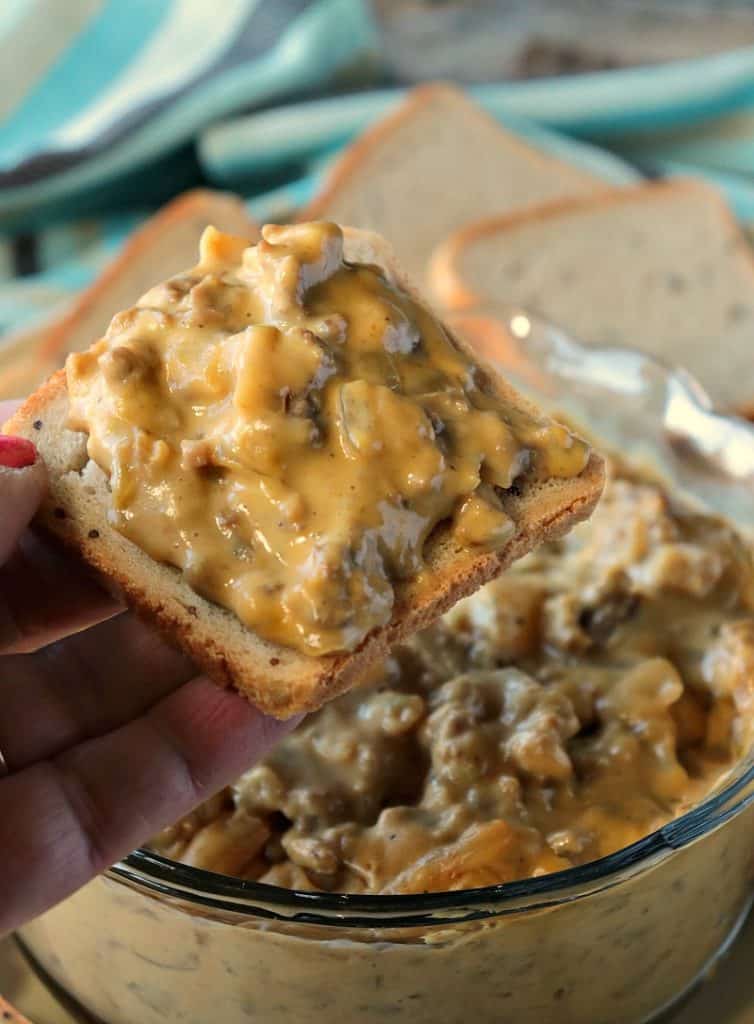 Closeup photo of a hand holding a cocktail party bread spread with cheesy patty melt dip.