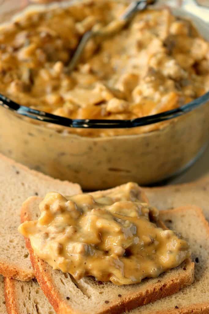 A closeup photo of patty melt dip on a small cocktail rye bread with a bowl of dip in the background.