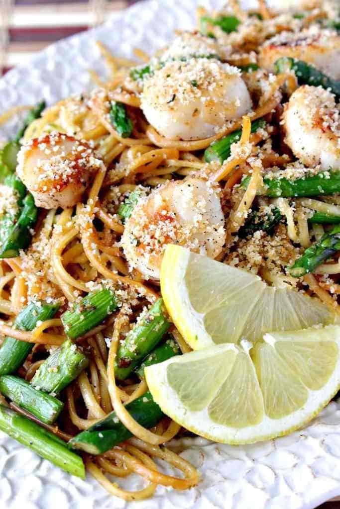 A closeup vertical photo of linguine with scallops, asparagus and buttered breadcrumbs. Valentine's Day dinner recipe roundup. 