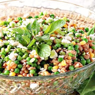 A clear glass bowl filled with Pea and Farro Salad along with a green napkin and fresh mint.