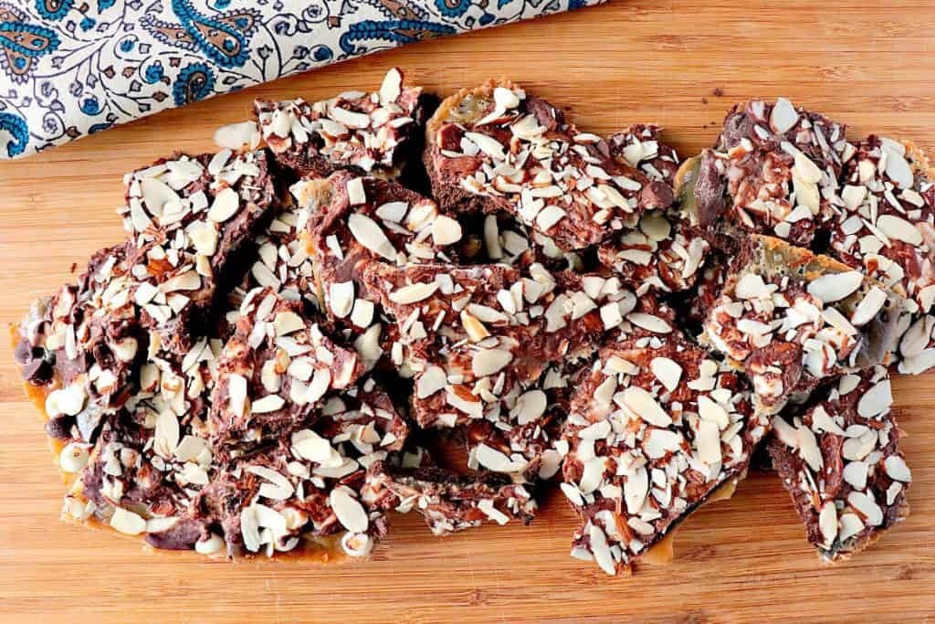 Double Chocolate Graham Cracker Toffee with Almonds on a wooden board with a blue and brown napkin.