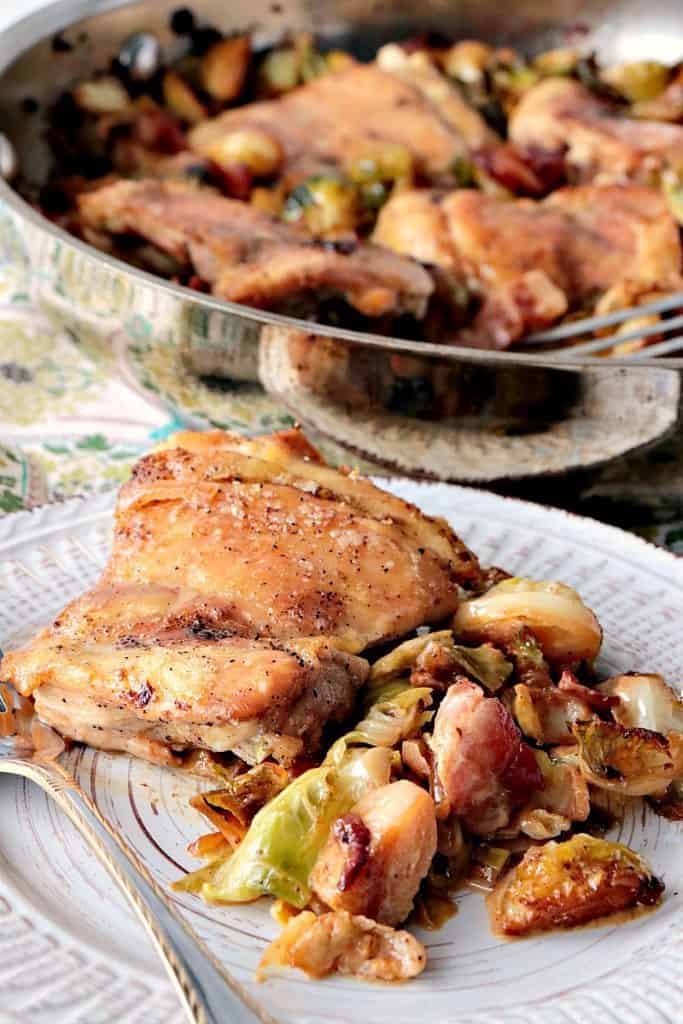 Closeup vertical photo of an easy chicken dinner recipe of chicken thighs with Brussels sprouts and bacon on a plate with a fork, and a skillet in the background.