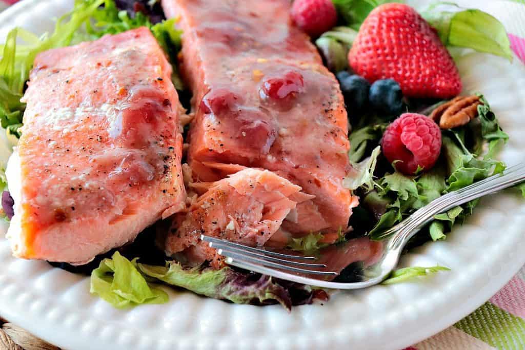 Flaky salmon filled with strawberry jam glaze, salad, and berries on a white plate.