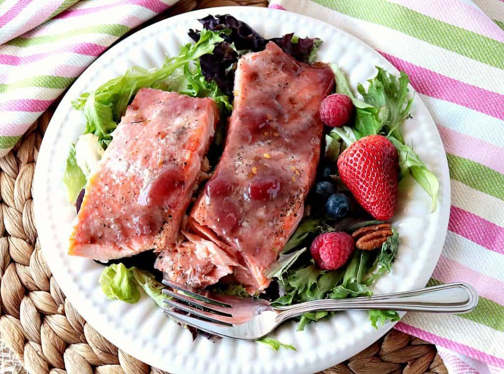 Overhead photo of strawberry glazed salmon fillets on a white plate with a salad and fresh berries.