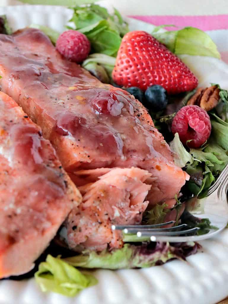 Closeup photo of flaked salmon on a white plate with a strawberry glaze.