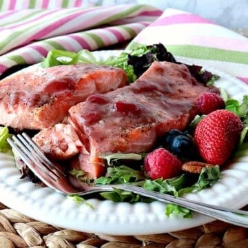 Strawberry Glazed Salmon fillets on a white plate with greens and berries.