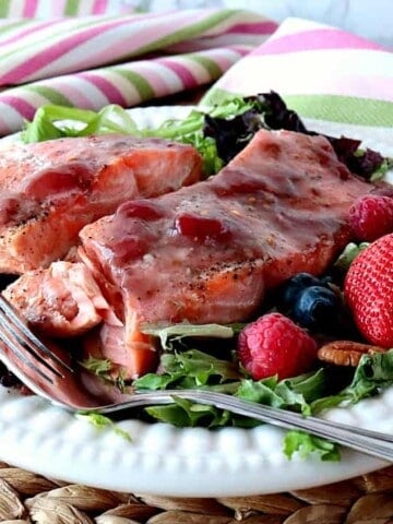 Strawberry Glazed Salmon fillets on a white plate with greens and berries.