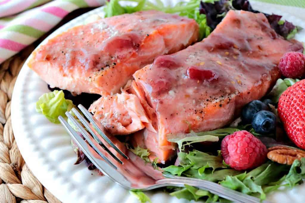 Flaky salmon fillets on a white plate with a fork, berries and greens.