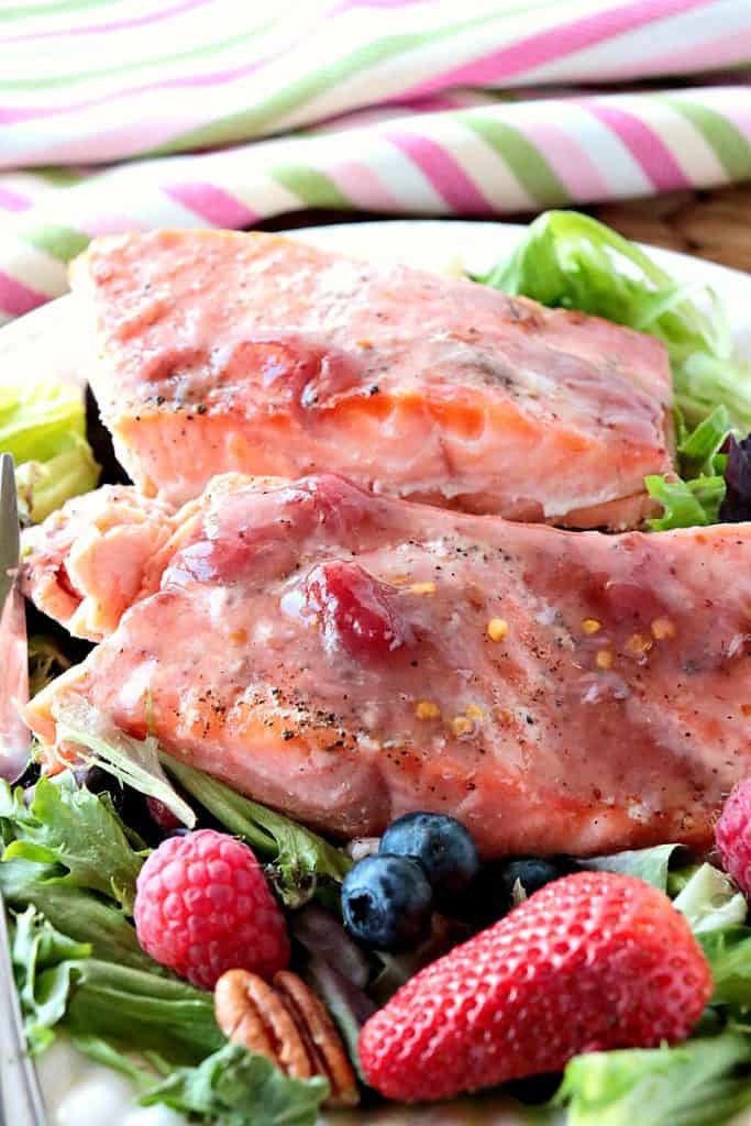 Closeup photo of a piece of jammin salmon on a plate with a salad and a pink and green striped napkin in the background.