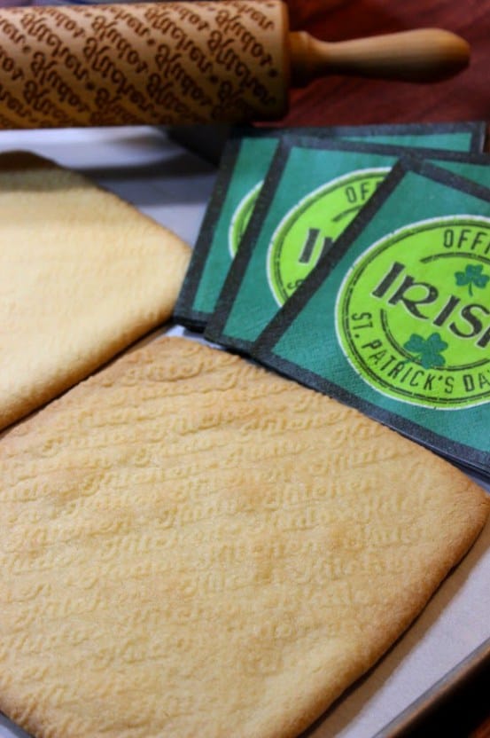 A closeup vertical image of traditional Irish shortbread cookies with Irish napkins and a rolling pin the the background.