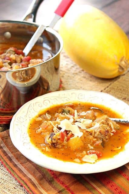 Vertical photo of a bowl of spaghetti squash soup with a pot and ladle in the background along with a whole spaghetti squash.
