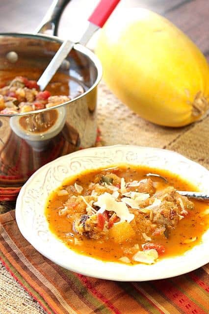 Vertical image of a bowl of spaghetti squash soup with a saucepan and a spaghetti squash in the background.