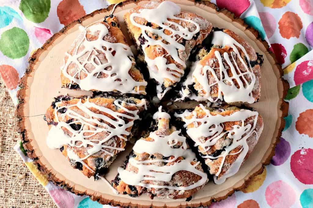 An overhead photo of a wood plate filled with Blueberry Lemon Scones drizzled with icing.