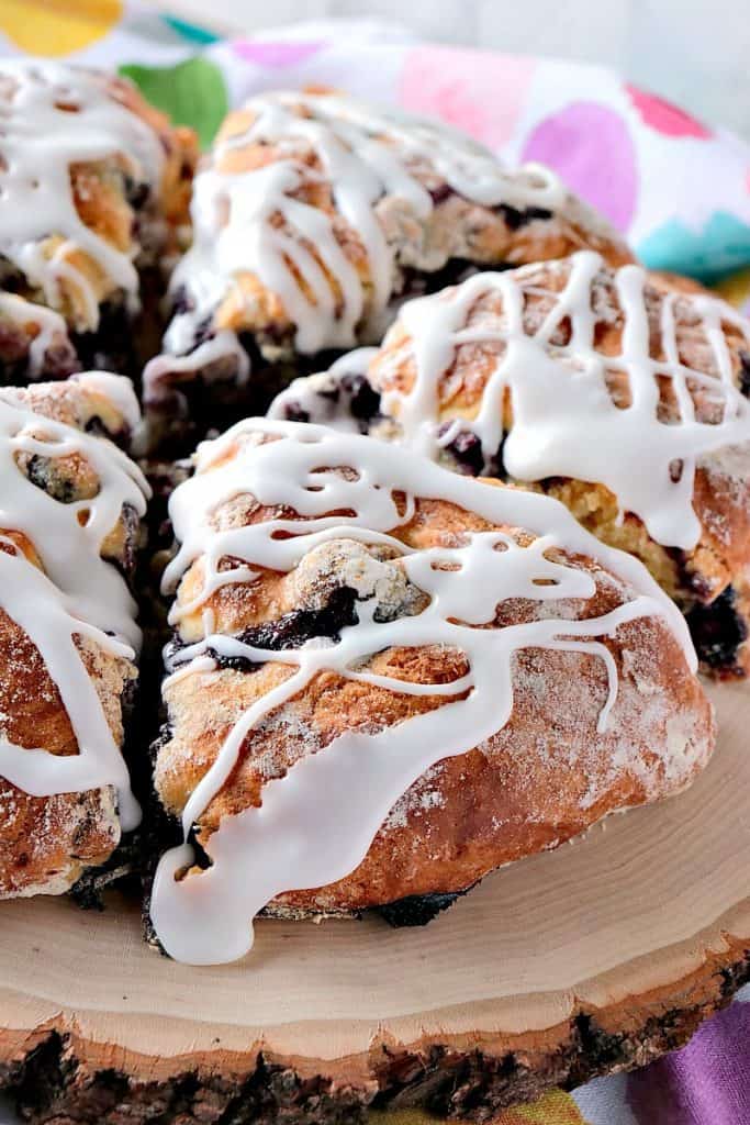 Vertical closeup picture of Blueberry Lemon Scones on a wooden platter with a thick layer of icing.