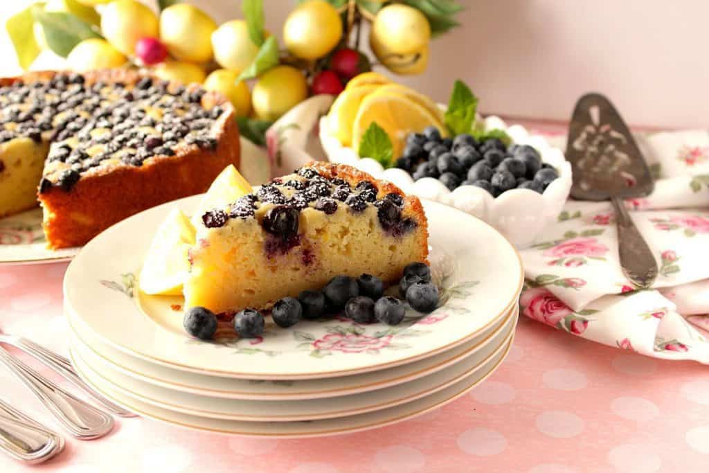 Slice of lemon ricotta cake on a stack of china plates on a pink tablecloth.