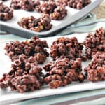 A white platter filled with Chocolate and Peanut Butter Granola Jumbles and a baking sheet with the jumbles in the background.
