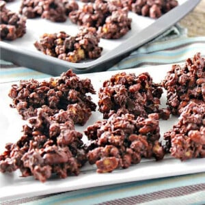 A white platter filled with Chocolate and Peanut Butter Granola Jumbles and a baking sheet with the jumbles in the background.