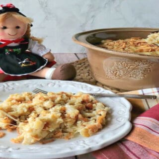 A German Spaetzle Casserole in a round tan dish with a little German doll in the background.
