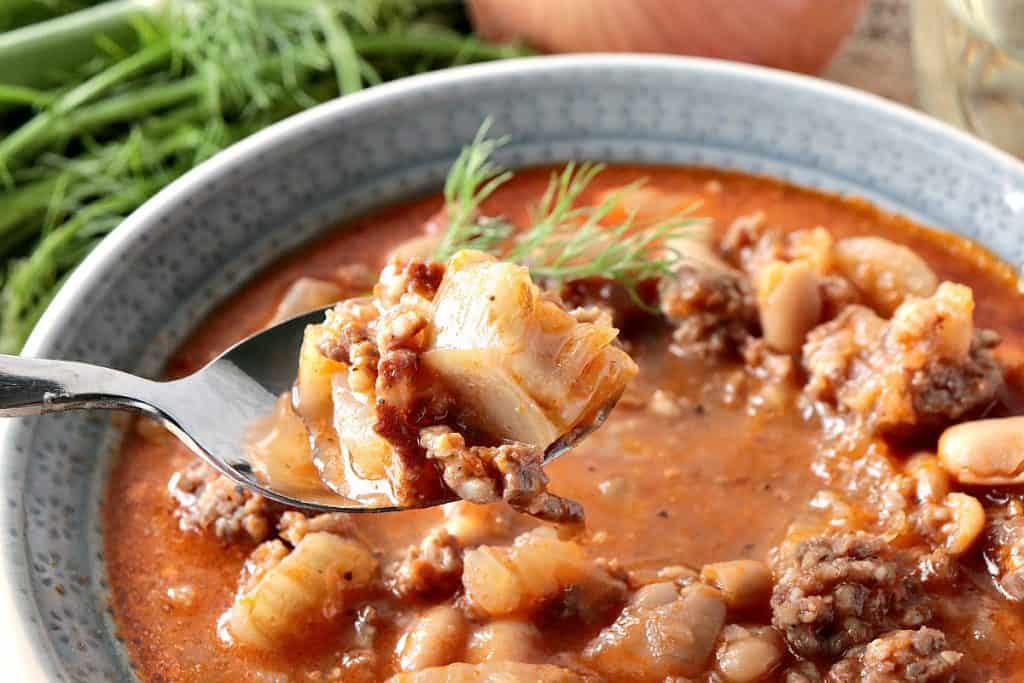 Closeup shot of White Bean, Fennel & Italian Sausage Soup on a spoon. - www.kudoskitchenbyrenee.com