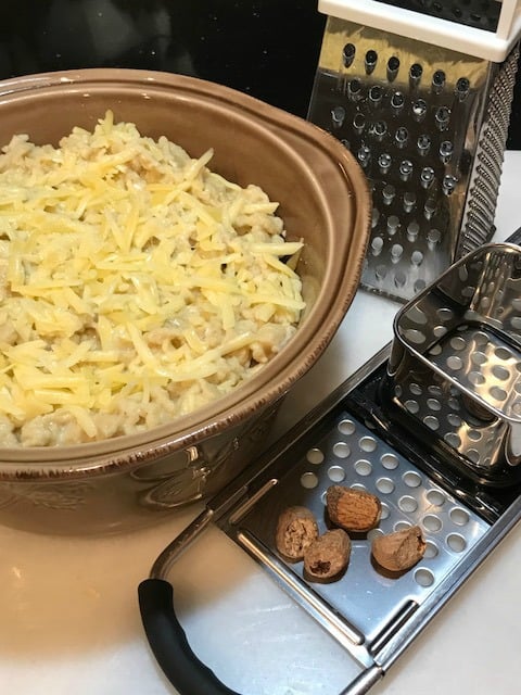 A vertical photo of a German spaetzle maker with grated nutmeg and a casserole with grated cheese on top.