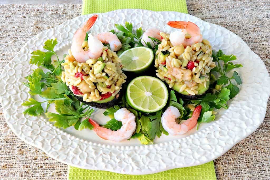 Orzo, Shrimp & Vegetable Salad Stuffed Avocados is an elegant dish which can be served for a light lunch or dinner option. Since it's served cold, it's the perfect refreshing and refined dish to make and enjoy during the hot summer months. - kudoskitchenbyrenee.com A pretty platter filled with two Orzo and Shrimp Stuffed Avocados with vegetables.