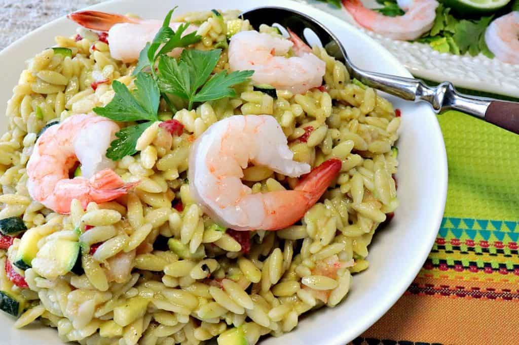 A white bowl filled with an orzo, avocado, and shrimp pasta salad.