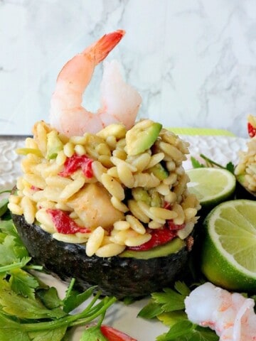 A cooked shrimp on top of an orzo salad stuffed into an avocado.