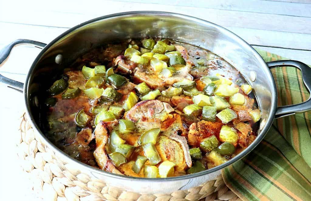 These fork-tender Dill Pickle Pork Chops with Bacon & Onion and infused with flavor from the pickle juice brine, the browned bacon, and sauteed onions. This fast and easy low-carb recipe will soon become a family favorite! - kudoskitchenbyrenee.com A silver skilled filled with pickles and pork chops.