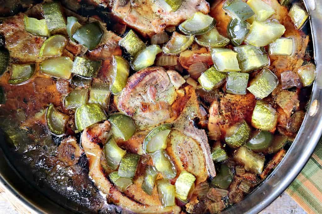Dill Pickle Pork Chops in a skillet with sauce and pickle chunks.