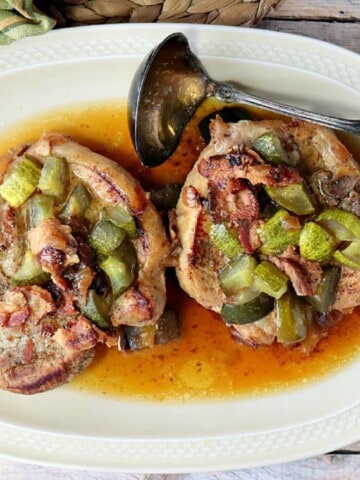 Two Dill Pickle Pork Chops on an oval platter with a ladle on the side.