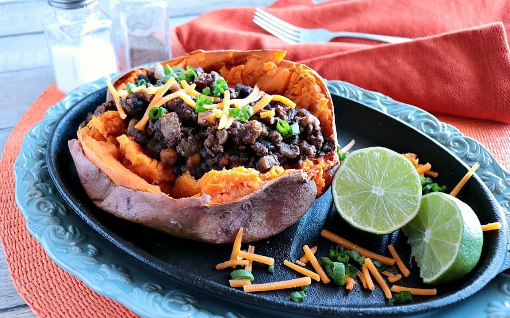 Spicy Tex-Mex Stuffed Sweet Potatoes on a blue platter with lime slices and cheddar cheese.