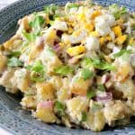 A blue bowl filled with Golden Dijon Potato Salad with chopped eggs and celery leaves as garnish.