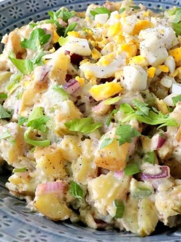 A blue bowl filled with Golden Dijon Potato Salad with chopped eggs and celery leaves as garnish.