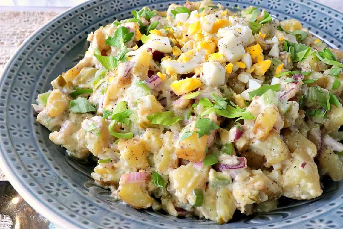 A blue bowl filled with Golden Dijon Potato Salad with chopped eggs and celery leaves as garnish.