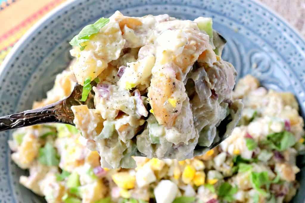 a horizontal closeup photo of a spoonful of creamy potato salad with hard cooked eggs, celery, and mayonnaise.