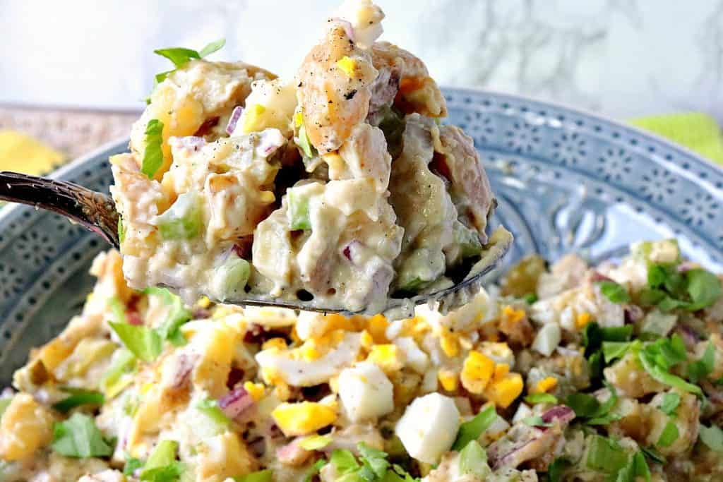 A spoon piled high with creamy Dijon potato salad.