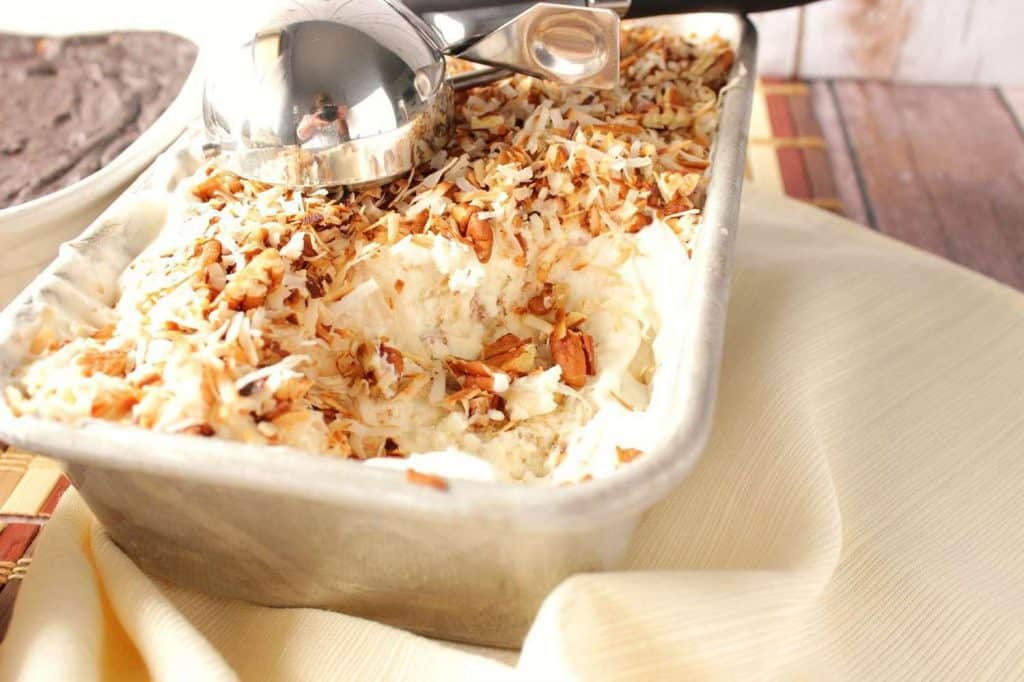 A loaf pan filled with Toasted Coconut Pecan No-Churn Ice Cream with an ice cream scoop included.