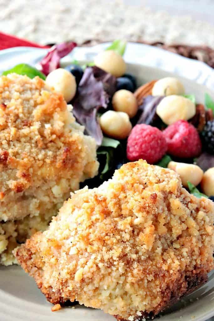 A closeup vertical image of two baked macadamia nut crusted chicken thighs with a salad with berries in the background.
