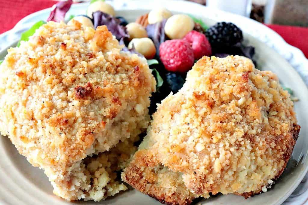 Closeup horizontal photo of two golden macadamia nut coated pieces of chicken thighs with a salad with berries and macadamia nuts on the same plate.