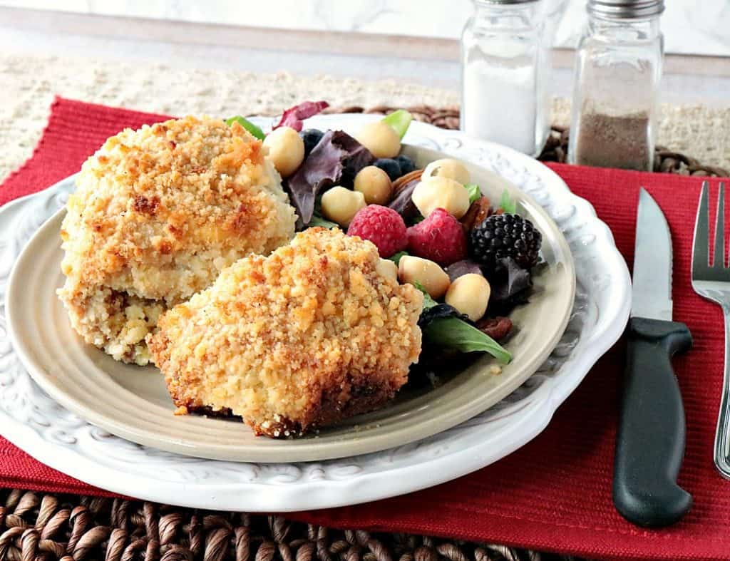 Keto approved macadamia nut coated chicken thighs on a plate with a red napkin, fork, knife, and a salt and pepper shaker.