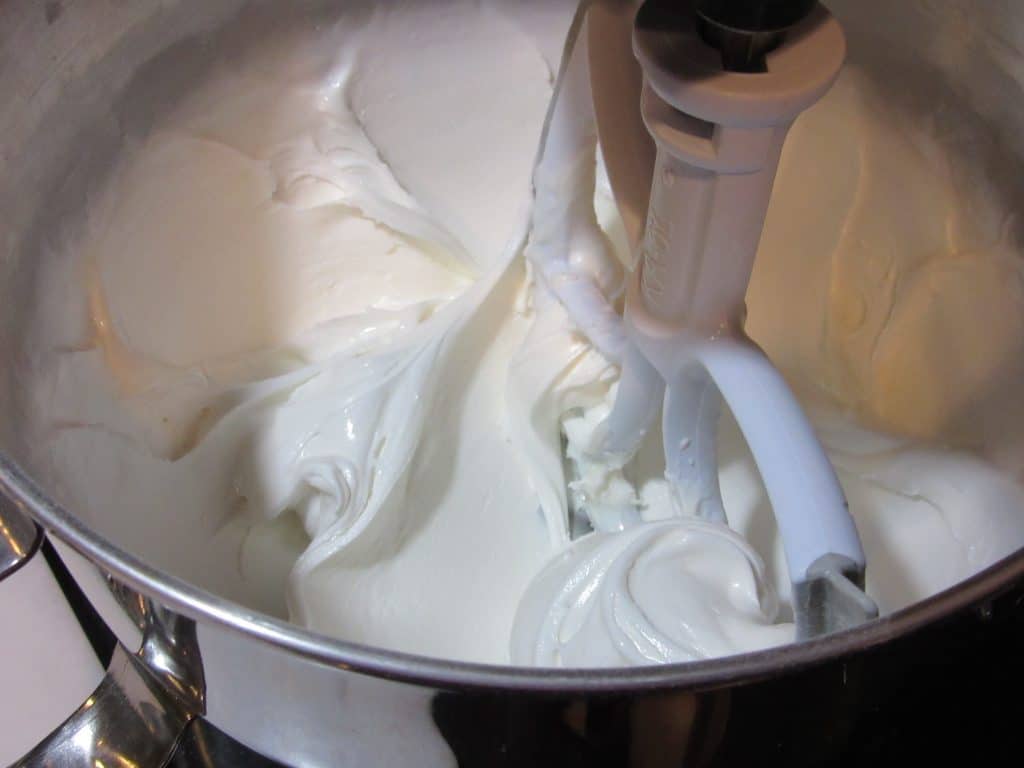 Closeup picture of royal icing in a mixing bowl with a paddle attachment.