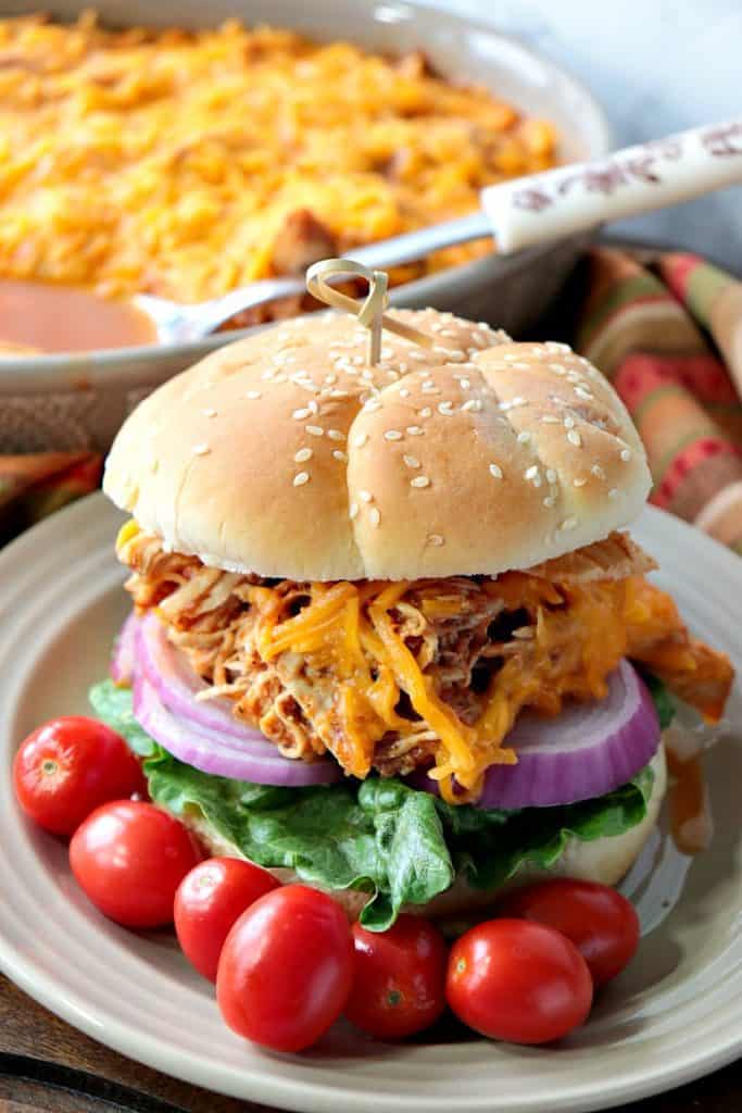 A closeup photo of shredded salsa chicken sandwich in the foreground with a casserole with a large spoon in the background.