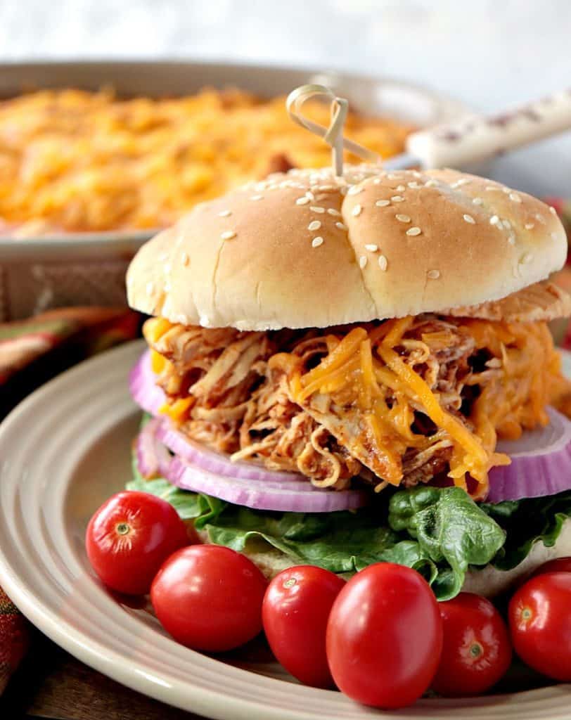 A closeup vertical photo of a shredded salsa chicken sandwich on a bun with red onion, lettuce, melted cheese and tomatoes.