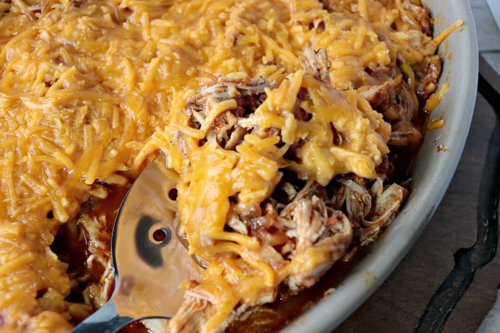Overhead closeup photo of a spoon inside a dish of shredded salsa chicken covered with melted cheese.