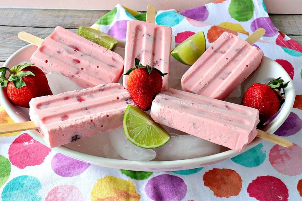 A horizontal photo of a colorful bowl of  strawberry keto popsicles with strawberries and lime wedges.
