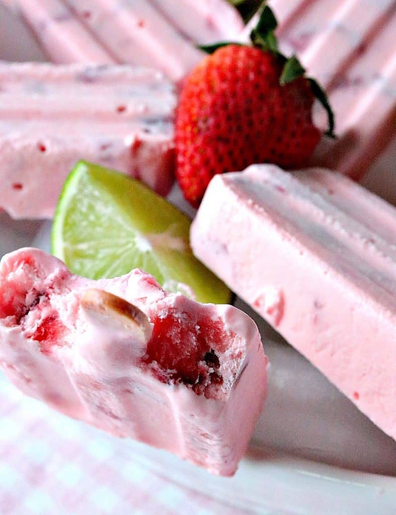 Frozen strawberry cream pops in a bowl with one having bites taken out.